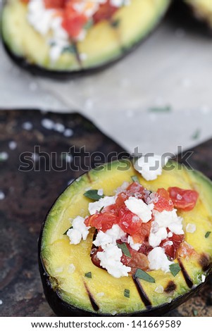 Grilled avocados filled with diced tomatoes and feta cheese and garnished with olive oil and freshly chopped parsley.