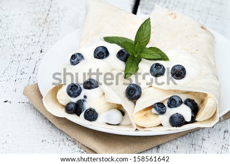 Breakfast burritos with fresh bananas, blueberries, and yogurt over a rustic wooden background.