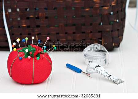 Red pincushion with sewing basket in the background. Shallow DOF.