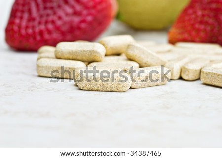 Prenatal vitamins with fresh fruit in the background. Shallow DOF with focus on front vitamin.