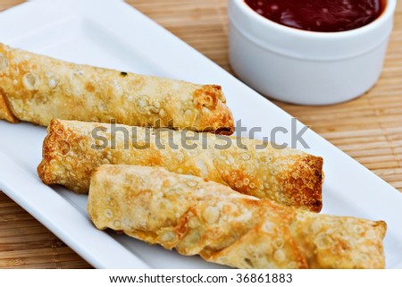 Deep fried golden egg rolls with sweet and sour sauce.  Selective focus on center egg roll.