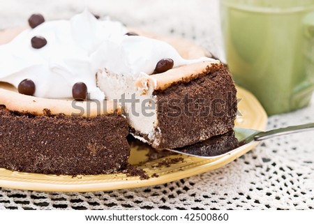 A slice of cheesecake with chocolate graham cracker crust being removed.