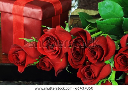 Up-close image of beautiful long stem red roses with gift in a breakfast tray on a bed.