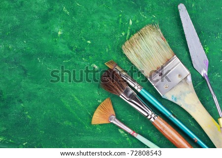 Artist paintbrushes and palette knife against an abstract grunge painting.