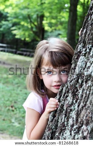 Little girl leaning against a large oak tree and looking at the viewer. Extreme shallow depth of field with selective focus on child. Some blur on tree.