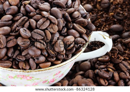 Cup filled with coffee beans over a background of whole and freshly ground coffee beans. Extreme shallow depth of field with selective focus on beans in cup.