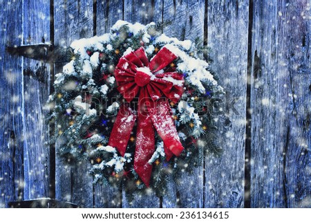 Rustic Christmas wreath on old weathered door with Christmas lights in a snow storm.