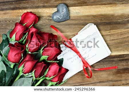 Long stem red roses with a stack of old letters tied with a red ribbon and card a little stone heart with the word love.