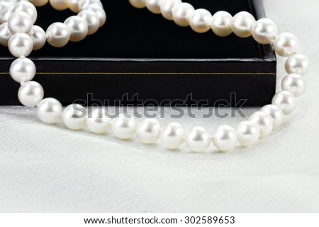 String of a beautiful pearl necklace lying over a black case. Extreme shallow depth of field.