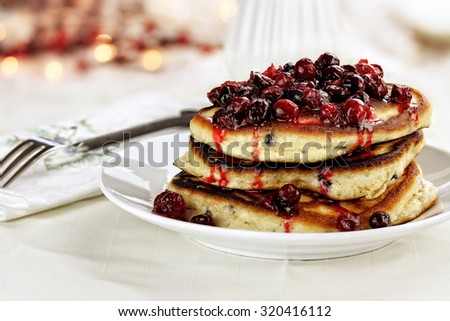 Cranberry sauce made with maple syrup, butter and fresh cranberries over delicious golden pancakes for Christmas morning. Extreme shallow depth of field with selective on pancakes.
