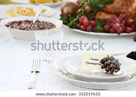 Thanksgiving Holiday table setting with cranberry sauce, deviled eggs and roast turkey in background. Happy Thanksgiving note card placed on plate. Extreme shallow depth of field.
