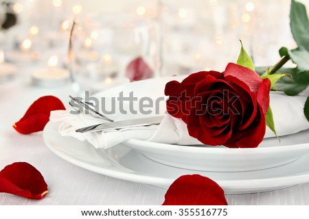Romantic candlelite table setting with long stem red rose. Shallow depth of field with selective focus on rose.