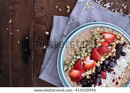 Hot breakfast of healthy oatmeal with shredded coconut, blackberries, blueberries, walnuts, heart shaped strawberries and pumpkin seeds over a rustic background. Image shot from overhead.