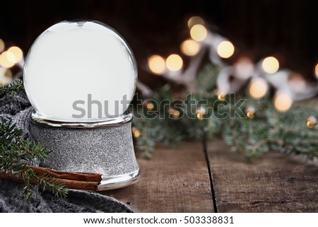 Rustic image of an empty Christmas snow globe surrounded by pine branches, cinnamon sticks and a warm gray scarf with copy space. Shallow depth of field with selective focus on snowglobe.