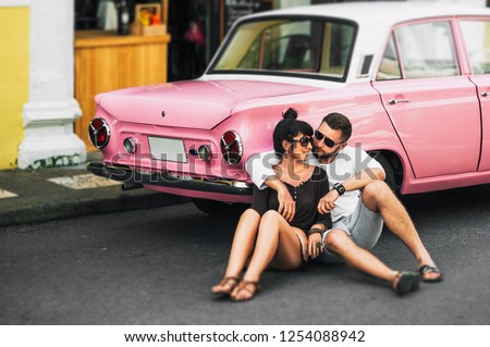 Couple in love hugging at the car. Couple resting on the car. Beautiful bearded man and attractive young woman in an old classic car. Stylish love story. Hugging and kissing in the car.