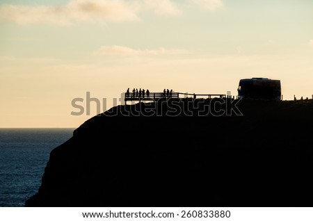 A silhouette of a tour bus parked on top of a cliff, overlooking the ocean. Image taken on Phillip Island, Australia on a summer evening.