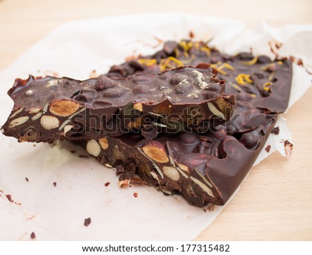 A smaller piece of fresh homemade rocky road chocolate on a bigger piece placed on white parchment paper against a wooden beige