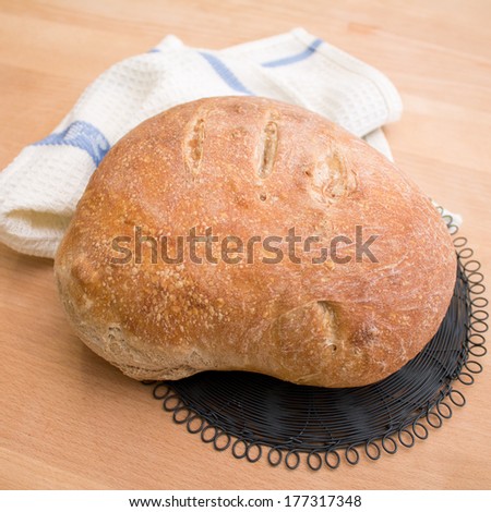 Fresh home baked loaf of bread on wooden table with white tablecloth and black vintage drying rack