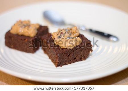 2 pieces of Fresh Homemade Vegan Chocolate Brownies topped with peanut butter and chia seeds with tiny spoon on beige plate on wooden table