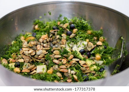Kale salad with pear, pumpkin seed, blueberry in silver salad bowl on white background