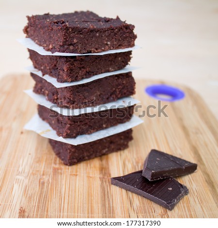 Fresh Homemade Vegan Chocolate Brownies stacked separated with parchment paper with two pieces of dark chocolate on the side on beige