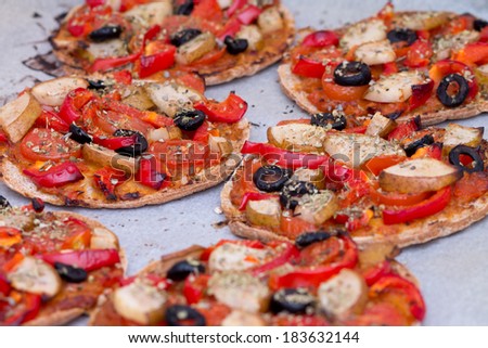 Home baked vegan mini pizza with olives, red pepper, tomato, pear, oregano and pesto on parchment paper
