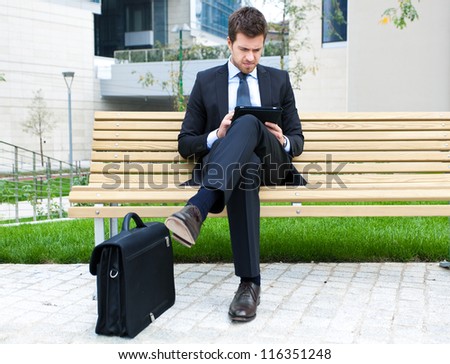Young businessman using a tablet on a bench in the city