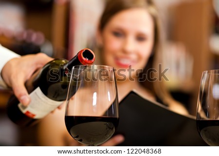 Waiter pouring red wine to a woman