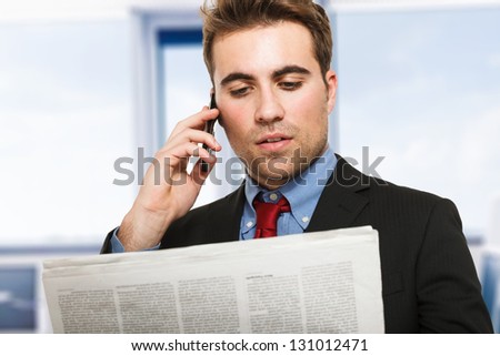 Young man talking on the phone while reading the newspaper