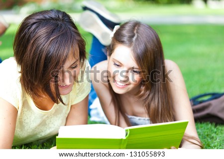 Two beautiful students reading a book on the grass