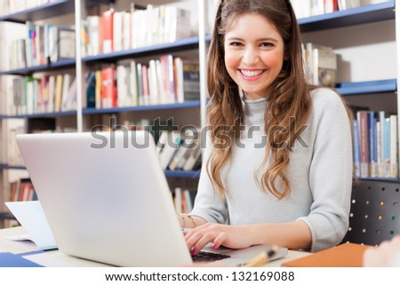 Portrait of a young smiling student using her laptop in a library