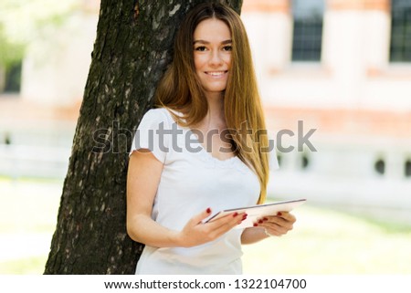 Young woman using a digital tablet lying against a tree in the park and enjoying the freedom of rhe wireless internet connection