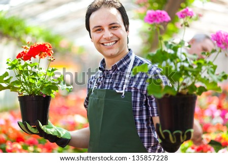 Happy Gardener In A Greenhouse Holding Two Vases Of Flowers