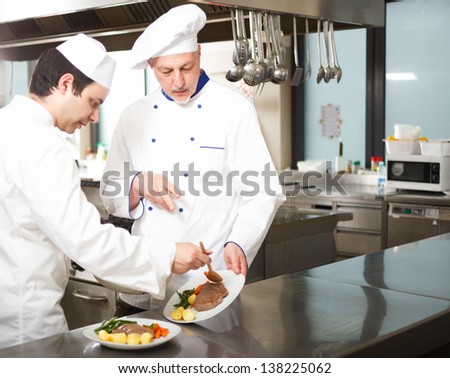 Chief chef watching his assistant garnishing a dish