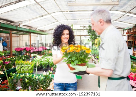 Portrait of a greenhouse worker giving a plant to a customer