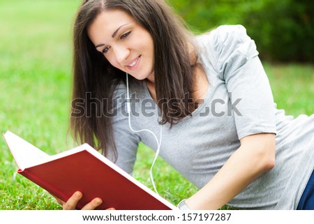 Woman reading a book and  listening music in a park