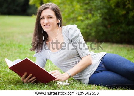 Woman reading a book and  listening music in a park