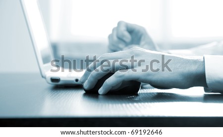 Closeup of male hands typing on a laptop and moving a mouse - blue toned image