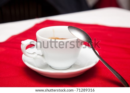 A white cup of coffee on a red table cloth