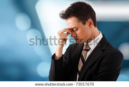 Young stressed and tired businessman. Blue blurred background.
