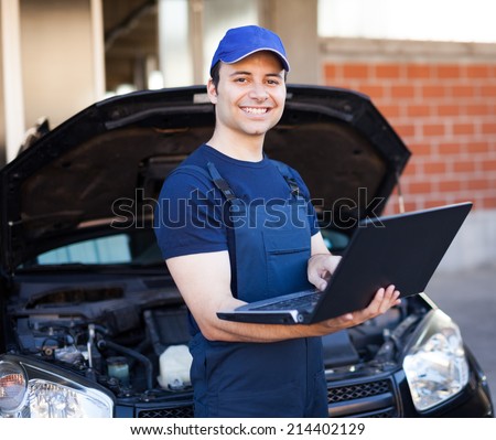 Smiling mechanic using a laptop computer to check a car engine