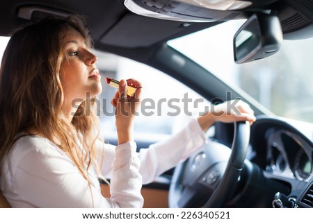 Woman using the rear-view mirror to apply make-up while driving her car