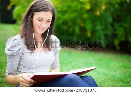 Woman reading a book while listening music in a park