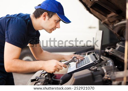 Skilled mechanic using a laptop computer to check a car engine