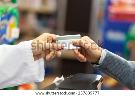 Hand of customer giving credit card to supermarket cashier at checkout