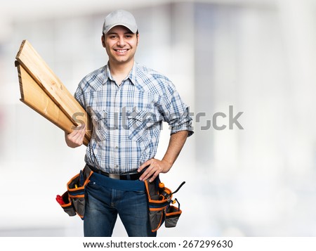Portrait of a smiling carpenter holding wood planks. Bright background