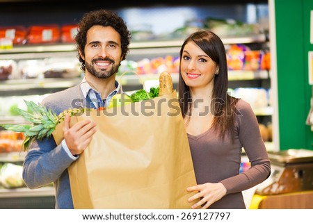 Couple holding a bag full of vegetables at supermarket