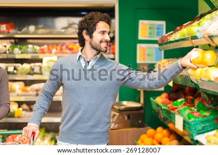 Smiling young man picking up vegetables in a grocery store