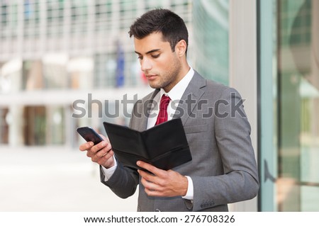 Portrait of a busy businessman using his mobile phone while holding an agenda