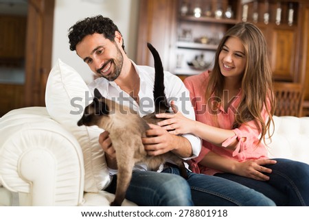 Portrait of an happy couple playing with their cat on the couch. Shallow depth of field, focus on the man